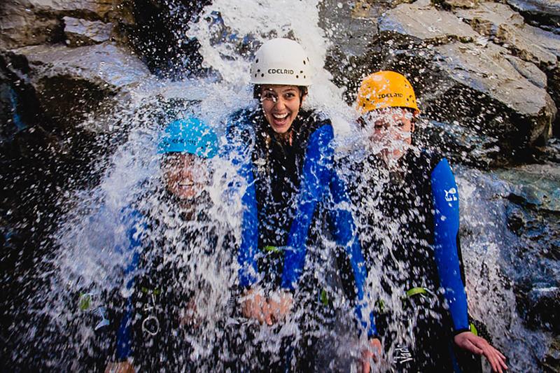 A picture of 3 people wearing helmets under a waterfall while canyoning in colorado